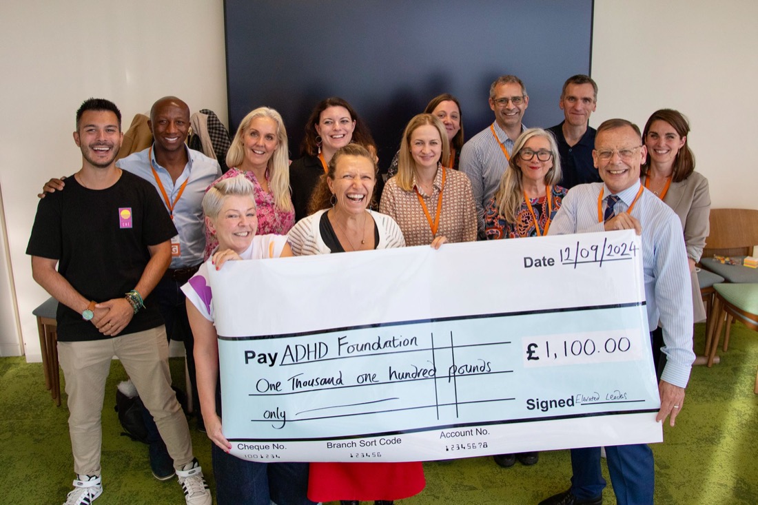 A group of about fourteen people holding a giant novelty cheque made out to the ADHD Foundation for £1,100.